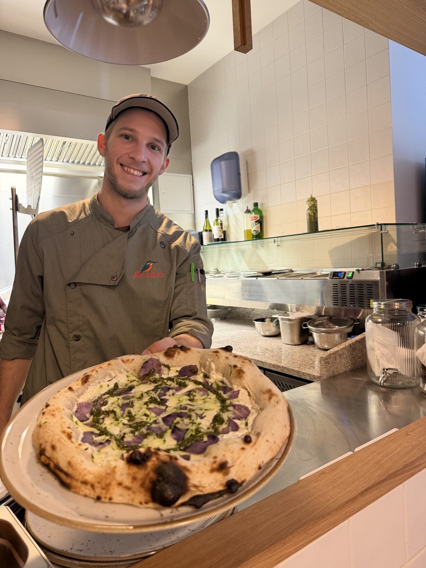 Pizzaiolo mit frisch gebackener Pizza in der Küche von Alcedo's Graz